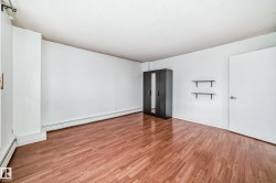 Spacious room featuring wood-finish flooring, white walls, and a textured white ceiling - 