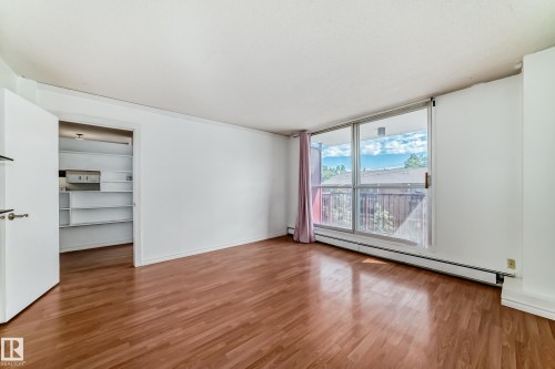 Living area featuring wood-finish flooring, white walls, and a full-height sliding glass door - 401 11007 83 Avenue, Edmonton, AB 