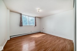 Spacious room featuring wood-finish flooring, a large window, white walls, baseboard heating, and a built-in closet with mirrored doors - 