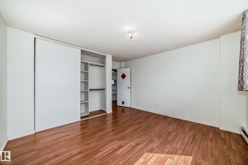 Bedroom featuring wood-finish flooring, white walls, and a built-in closet with sliding doors and integrated shelving - 401 11007 83 Avenue, Edmonton, AB 