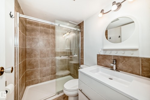 Full bathroom featuring a tub-shower combination with sliding glass doors, brown tile surround, and a built-in shelf - 401 11007 83 Avenue, Edmonton, AB 