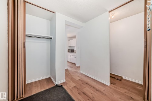 Entryway featuring wood-finish flooring, white baseboards, and two storage closets with accordion doors - 401 11007 83 Avenue, Edmonton, AB 