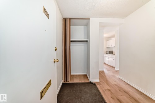 Entryway featuring wood-finish flooring, a coat closet with shelving and hanging rod, and a white interior door with brass hardware - 401 11007 83 Avenue, Edmonton, AB 