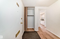 Entryway featuring wood-finish flooring, a coat closet with shelving and hanging rod, and a white interior door with brass hardware - 