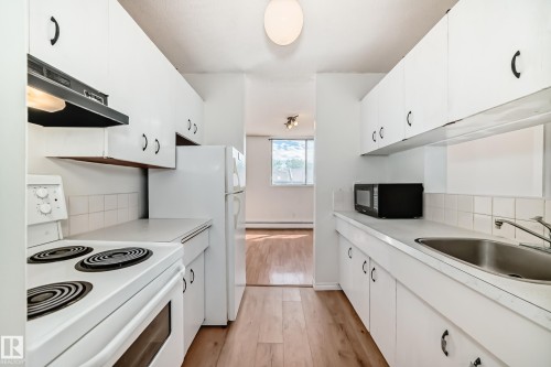 Galley kitchen featuring white cabinetry, a built-in range hood, and a white tile backsplash - 401 11007 83 Avenue, Edmonton, AB 