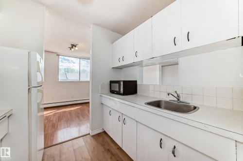 Kitchen featuring white cabinetry, a stainless steel sink, white tiled backsplash, and white countertop - 401 11007 83 Avenue, Edmonton, AB 