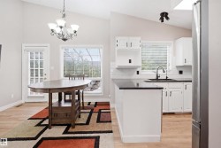 Vaulted ceiling kitchen featuring white cabinetry, a black countertop island, stainless steel refrigerator, and a white subway tile backsplash - 