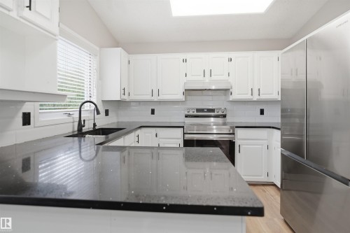 Kitchen featuring dark countertops, white cabinetry, a black faucet, stainless steel appliances, and wood-finish flooring - 3220 42A Avenue, Edmonton, AB 