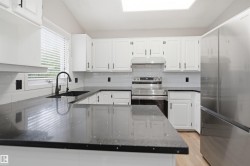 Kitchen featuring dark countertops, white cabinetry, a black faucet, stainless steel appliances, and wood-finish flooring - 