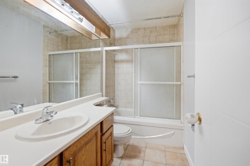 Bathroom featuring a wood-finish vanity with an integrated sink, a large mirror, and a shower-tub combination with sliding frosted glass doors - 3220 42A Avenue, Edmonton, AB 