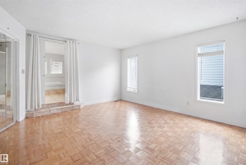 Spacious room featuring wood-finish parquet flooring, multiple windows with blinds, and a mirrored sliding closet door - 3220 42A Avenue, Edmonton, AB 