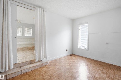 Bedroom featuring parquet wood-finish flooring, a window with horizontal blinds, and direct access to a separate bathing area - 3220 42A Avenue, Edmonton, AB 