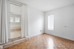Bedroom featuring parquet wood-finish flooring, a window with horizontal blinds, and direct access to a separate bathing area - 