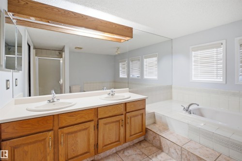 Bathroom featuring a dual vanity with wood cabinetry, a large built-in mirror, a tiled soaking tub, and multiple windows with blinds - 3220 42A Avenue, Edmonton, AB 
