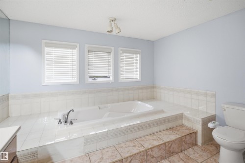 Spacious bathroom featuring an integrated soaking tub with chrome fixtures, surrounded by white ceramic tiling - 3220 42A Avenue, Edmonton, AB 