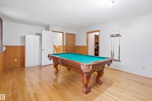 Entertainment room with wood-finish flooring, half-wall wood paneling, white walls, and a textured white ceiling - 3220 42A Avenue, Edmonton, AB 