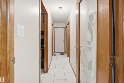 Hallway featuring white square tile flooring, light wood-finish door frames, a white ceiling with a flush-mount light fixture, and a door with frosted glass detailing - 3220 42A Avenue, Edmonton, AB 