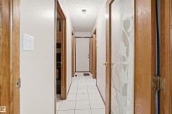Hallway featuring white square tile flooring, light wood-finish door frames, a white ceiling with a flush-mount light fixture, and a door with frosted glass detailing - 