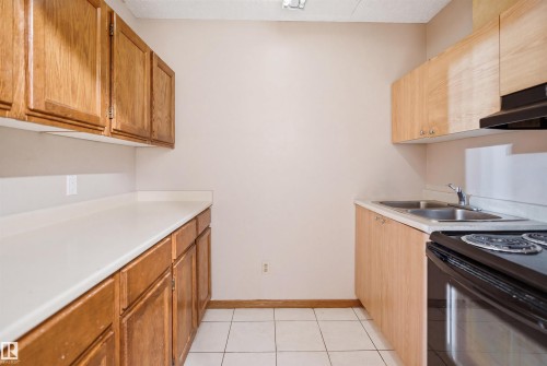 Galley kitchen featuring light wood-finish cabinetry, white countertops, double basin stainless steel sink, and a black electric range with a coordinating range hood - 3220 42A Avenue, Edmonton, AB 