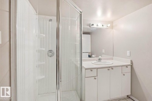 Bathroom featuring a glass-enclosed shower, white vanity with integrated sink, white countertop, and wall-mounted mirror with vanity lighting - 3220 42A Avenue, Edmonton, AB 