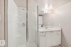 Bathroom featuring a glass-enclosed shower, white vanity with integrated sink, white countertop, and wall-mounted mirror with vanity lighting - 