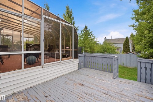 Rear exterior featuring a sunroom with large glass panels, a wooden deck, and a fenced backyard with mature trees - 3220 42A Avenue, Edmonton, AB 