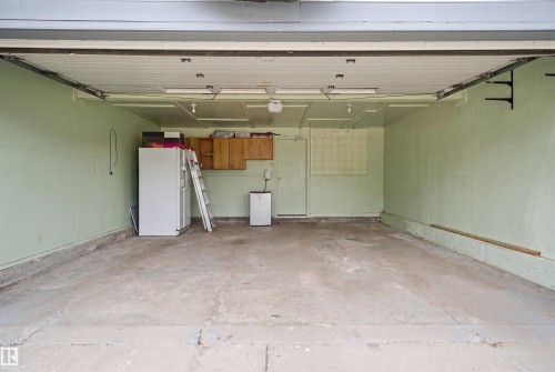 Concrete-floored garage featuring painted walls, overhead lighting, an interior access door, and upper cabinetry - 3220 42A Avenue, Edmonton, AB 