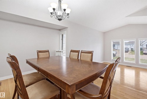 Dining area featuring hardwood flooring, a vaulted ceiling, a chandelier, and multiple windows with blinds - 3220 42A Avenue, Edmonton, AB 
