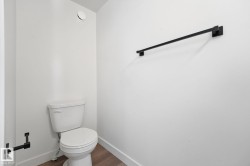 Contemporary powder room featuring a white toilet, wood-finish flooring, and matte black fixtures including a towel bar and toilet paper holder - 