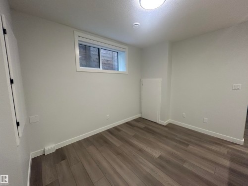 Room featuring wood-finish flooring, white baseboards, a single window, an overhead light fixture, and light-colored walls - 11012 132 Street, Edmonton, AB 