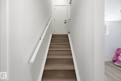 Staircase with wood-finish treads and risers, white walls, and a white handrail with black brackets - 
