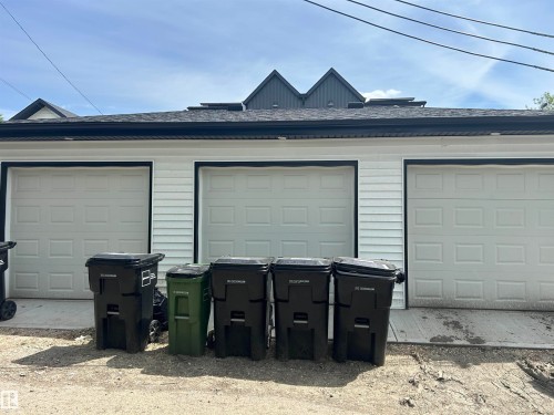 Three-car garage featuring white paneled doors with black trim, white horizontal siding, and a dark shingle roof - 11012 132 Street, Edmonton, AB 