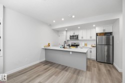 Contemporary kitchen featuring stainless steel appliances, white cabinetry, a white subway tile backsplash, a center island with a sink, and wood-finish flooring - 