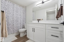 Bathroom featuring a white shaker-style vanity with matte black hardware, a light-toned countertop, a frameless mirror, and wood-finish flooring - 