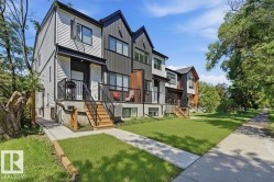 Modern townhouse exterior featuring contrasting light and dark siding, a private balcony with black railings, a concrete sidewalk, and a manicured lawn - 