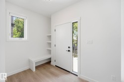 Entryway featuring a solid white door with a vertical window pane, natural wood-finish flooring, a built-in storage bench, integrated shelving, and a single recessed light fixture - 