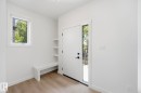 Entryway featuring a solid white door with a vertical window pane, natural wood-finish flooring, a built-in storage bench, integrated shelving, and a single recessed light fixture - 11012 132 Street, Edmonton, AB 