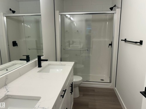 Bathroom featuring a double vanity with stone-finish countertop, dual integrated sinks, and matte black fixtures - 11012 132 Street, Edmonton, AB 