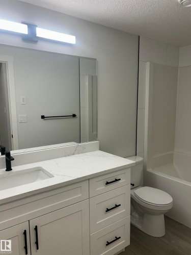 Bathroom featuring a white vanity with quartz countertop, integrated sink, and matte black fixtures - 11007 132 Street, Edmonton, AB 