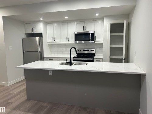Modern kitchen featuring a central island with a white countertop and integrated sink - 11007 132 Street, Edmonton, AB 