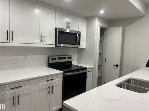 Modern kitchen featuring white shaker-style cabinetry with matte black hardware, stainless steel appliances, white subway tile backsplash, and light-colored countertops with integrated double basin sink - 11007 132 Street, Edmonton, AB 