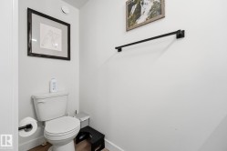 Powder room featuring light wood-finish flooring, a white toilet with a round bowl, and a wall-mounted matte black toilet paper holder - 
