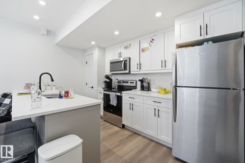 Contemporary kitchen featuring white shaker cabinetry with dark hardware, stainless steel appliances, and wood-finish flooring - 11007 132 Street, Edmonton, AB 