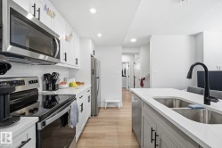 Contemporary kitchen featuring stainless steel appliances, white subway tile backsplash, light wood-finish flooring, and an island with an undermount double-basin sink and matte black faucet - 