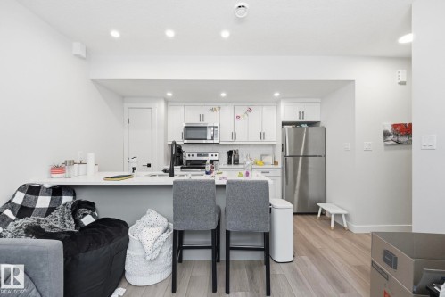 Open-concept kitchen featuring white cabinetry, stainless steel appliances, and a light-toned wood-finish flooring - 11007 132 Street, Edmonton, AB 