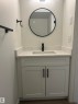 Bathroom vanity featuring white shaker-style cabinetry, a stone countertop with an integrated sink, a matte black faucet, and a circular mirror with a black frame - 11007 132 Street, Edmonton, AB 