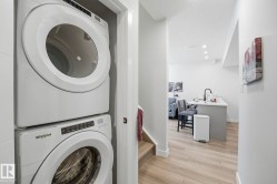 Dedicated laundry closet featuring a stackable washer and dryer, wood-finish flooring, recessed lighting, and a kitchen island with a dark faucet - 