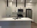 Kitchen featuring a large island with an undermount sink, white shaker cabinetry, stainless steel appliances, subway tile backsplash, and contemporary pendant lighting - 11007 132 Street, Edmonton, AB 