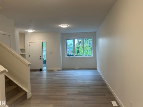 Spacious main level featuring light wood-finish flooring, a large window providing natural illumination, and built-in shelving - 11007 132 Street, Edmonton, AB 