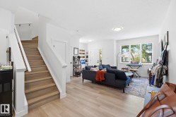 Open-concept living space featuring light wood-finish flooring, white walls, and a prominent staircase with white risers and wood treads - 
